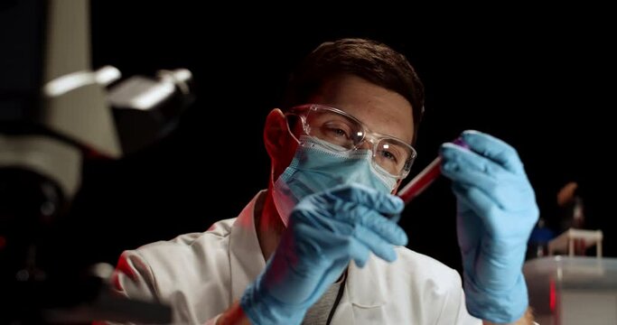 Doctor Examing Blood Test in Flusk in Laboratory. Laboratory Worker with Blood Sample. Covid Test. Blood Test. Man Working wearing Medical Mask, Glasses and Gloves.