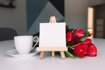 Bouquet of red tulips, coffee cup, empty white frame. Concept for greeting card