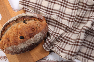 Obraz na płótnie Canvas Rustic whole grain artisan bread loaf with cranberry raisin dry fruit nuts wrapped in checkers cloth with wooden chopping board over table top flat lay view