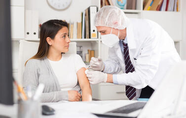 Obraz premium Doctor in white coat and protective mask giving vaccine injection to woman manager in office