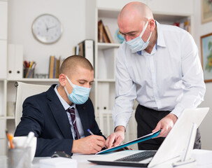 Businessman in protective face mask discussing project with colleague in white modern office