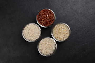 Long grain basmati medium grain jasmine short grain pilaf polau risotto brown low glycaemic index gi rice in small glass bowl wooden spoon on black background copy text space top flat lay view