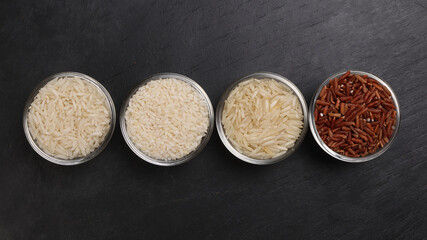 Long grain basmati medium grain jasmine short grain pilaf polau risotto brown low glycaemic index gi rice in small glass bowl wooden spoon on black background copy text space top flat lay view