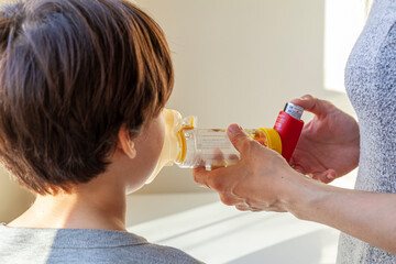A caucasian woman is giving emergency asthma medication to a small kit during an attack. She uses aerosol chamber with valve mask to deliver bronchodilators or corticosteroids to relieve symptoms.
