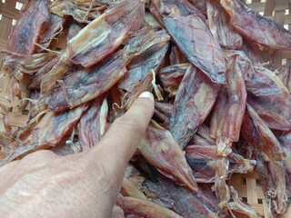 Finger pointing to dried squid, seafood in wicker basket closeup.