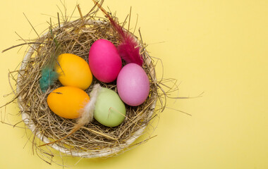 flat lay, colored easter eggs in a nest on a yellow background with a copy of the space