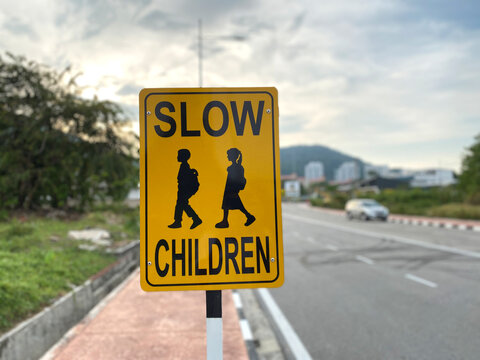 Close up view of a yellow road sign with "SLOW CHILDREN" which reminds vehicles to reduce speed due to school children