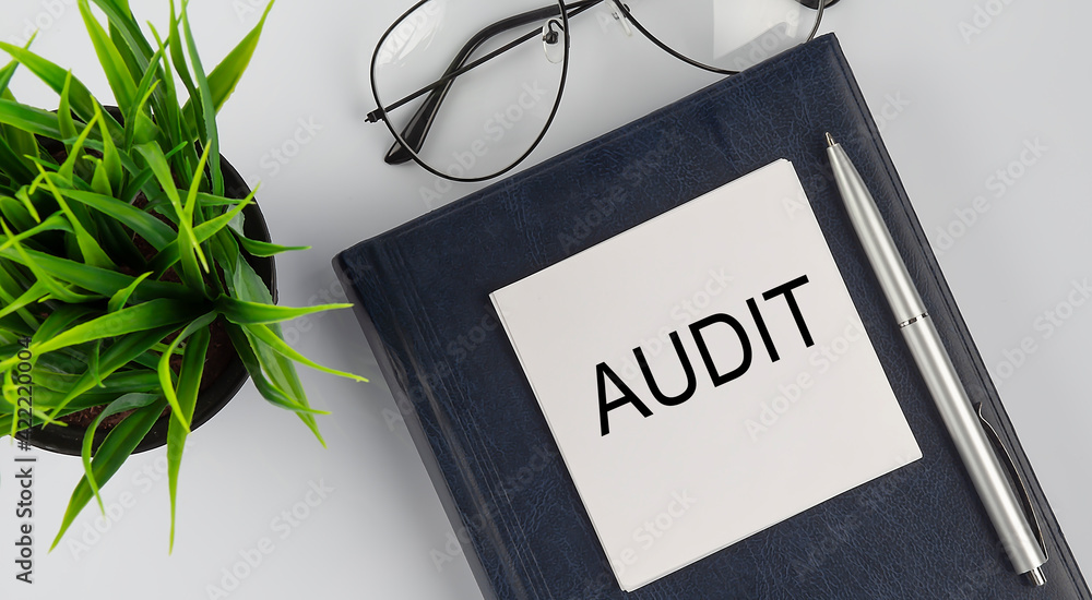 Poster stickers on notebook text audit with pen and glasses on white background
