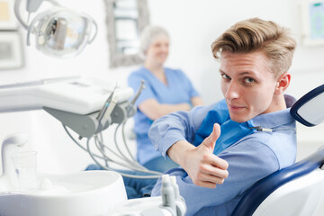 Portrait of satisfied man visiting dentist giving thumbs up in the dental clinic. High quality photo
