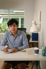 Portrait of young asian businessman sitting at home office and looking at camera.