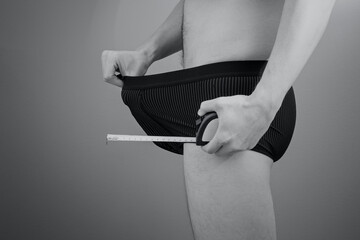 Adult caucasian man pulling his boxers with a hand, holding a tape measure in other hand. Concept...