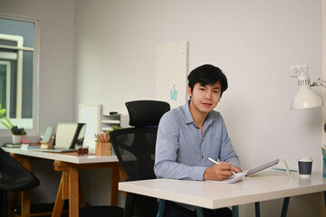 Smart businessman holding digital tablet and smiling to camera while sitting at home office.