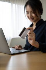Portrait of happy young woman holding credit card and using computer laptop for online payment or online shopping.