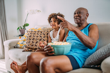 grandfather watching tv at home with grandson, eating popcorn