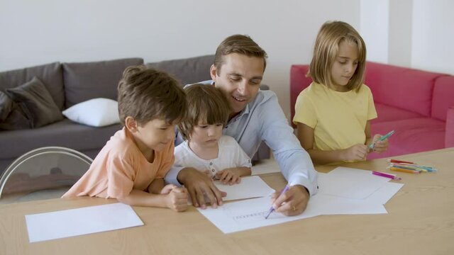 Smiling dad talking with kids and drawing with marker on paper. Caucasian father drawing with pen and playing with children in living room. Hand-held camera. Fatherhood and family time concept