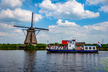 Kinderdijk, Netherlands - June 22, 2019: Tourist boat navigating the canals at Kinderdijk, Netherlands, with a traditional Dutch windmill in the background - 422222823