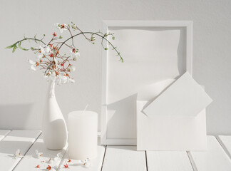 Mock up white invitation card,poster frame,candle and beautiful Nodding Clerodendron flowers in eramic vase on wood table white room interior,greeting card in soft tone still life