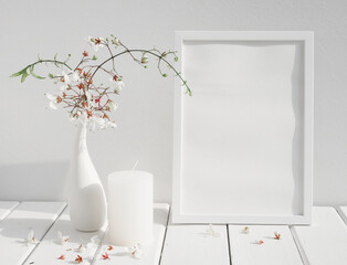 Mock up white invitation poster frame,candle and beautiful Nodding Clerodendron flowers in ceramic vase on wood table white room interior,greeting card in soft tone still life