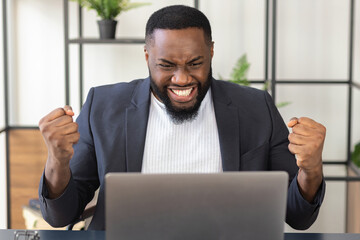 Happy African American male businessman in suit looking at the laptop happily, got a good message or made a good deal