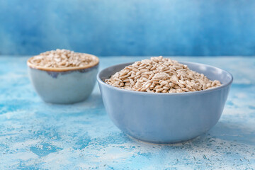 Bowls with sunflower seeds on color background