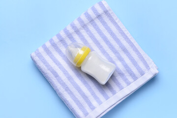 Bottle of milk for baby and towel on color background