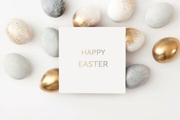 Golden and gray eggs with a paper white card on a white background. Minimal easter concept.