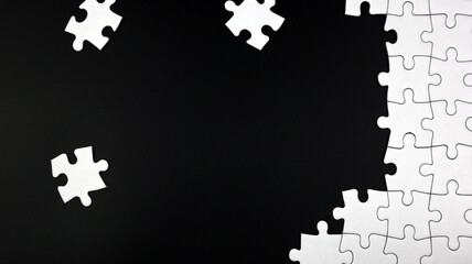 Unfinished white jigsaw puzzle pieces on black background