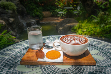 A set of hot coffee drinks placed on a ceramic table. The backdrop of a waterfall, lush greenery, and steam floated out to make it look fresh..