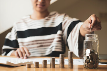 Woman's hand. Put a coin into a glass bottle with coins, saving money with coins, stepping into a successful growing business, and saving for thought in retirement. Retirement savings concept