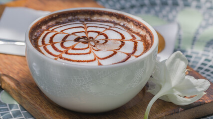 Chic design on hot coffee in white hot coffee mug, placed on a ceramic table. .The backdrop of a waterfall, lush greenery, and steam floated out to make it look fresh..