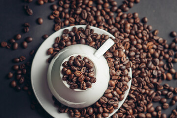 coffee beans on a saucer and an inverted white cup on a dark background female hands
