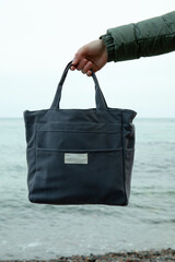 Female hand hold stylish eco bag against sea