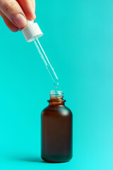 Female hand holding dropper over bottle of serum on blue background.