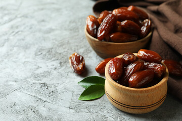 Bowls of dried dates and kitchen napkin on gray textured background