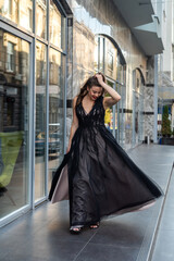 Naklejka premium incredibly beautiful full-length woman posing among the city in an amazing black evening dress.