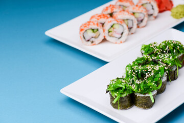 Japanese sushi with rice and fish and seaweed salad on top. Served on a white plate over blue background.