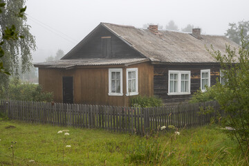 Old wooden house behind a fence. View of the village house. Everyday life in the countryside. Foggy...