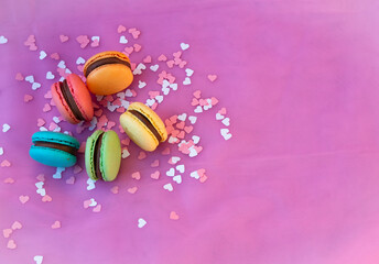 Multicolored macarons with pink and white hearts on a pink background.