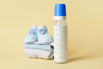 Bottle of milk for baby and clothes on color background