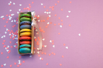 Multicolored macarons in a paper box and multicolored sweets on a romantic background.