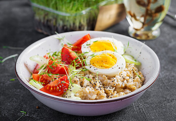 Breakfast oatmeal porridge with boiled egg, cherry tomatoes, celery and microgreens. Healthy balanced food.