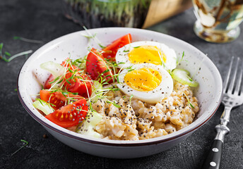 Breakfast oatmeal porridge with boiled egg, cherry tomatoes, celery and microgreens. Healthy balanced food.