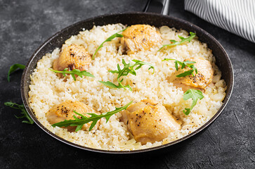 Rice with chicken thighs, pilaf  in skillet on dark background.