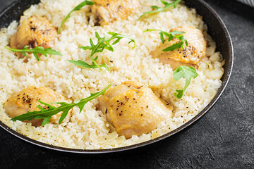Rice with chicken thighs, pilaf  in skillet on dark background.