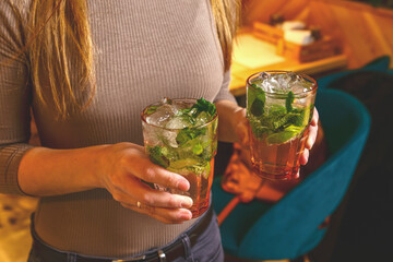 Two Mojito drinks in hands of a young woman. Partying concept, drinking Mojito in a bar.