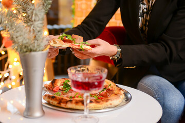 Image of young woman hand taking slice of pizza in restaurant or diner during Christmas holidays.