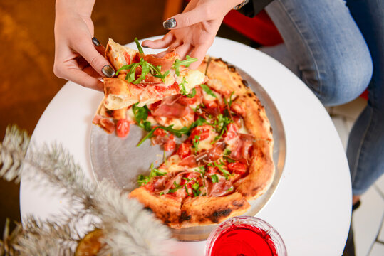 Image of young woman hand taking slice of pizza in restaurant or diner during Christmas holidays.