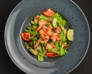 Rare fried salmon steaks in fresh vegetable salad. Delicious dinner, healthy food concept. Over black background.