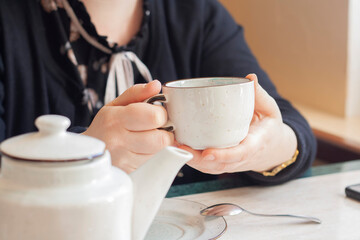 White cup of tea in the hands of a woman, teapot, restaurant