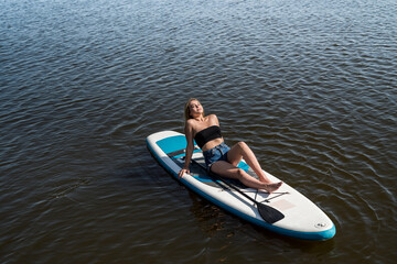 Young female surfer lying on sup board and rest at nature